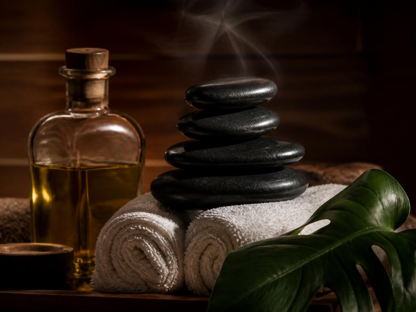 Batu vulkanik hitam hangat tersusun di atas handuk putih di samping minyak massage
