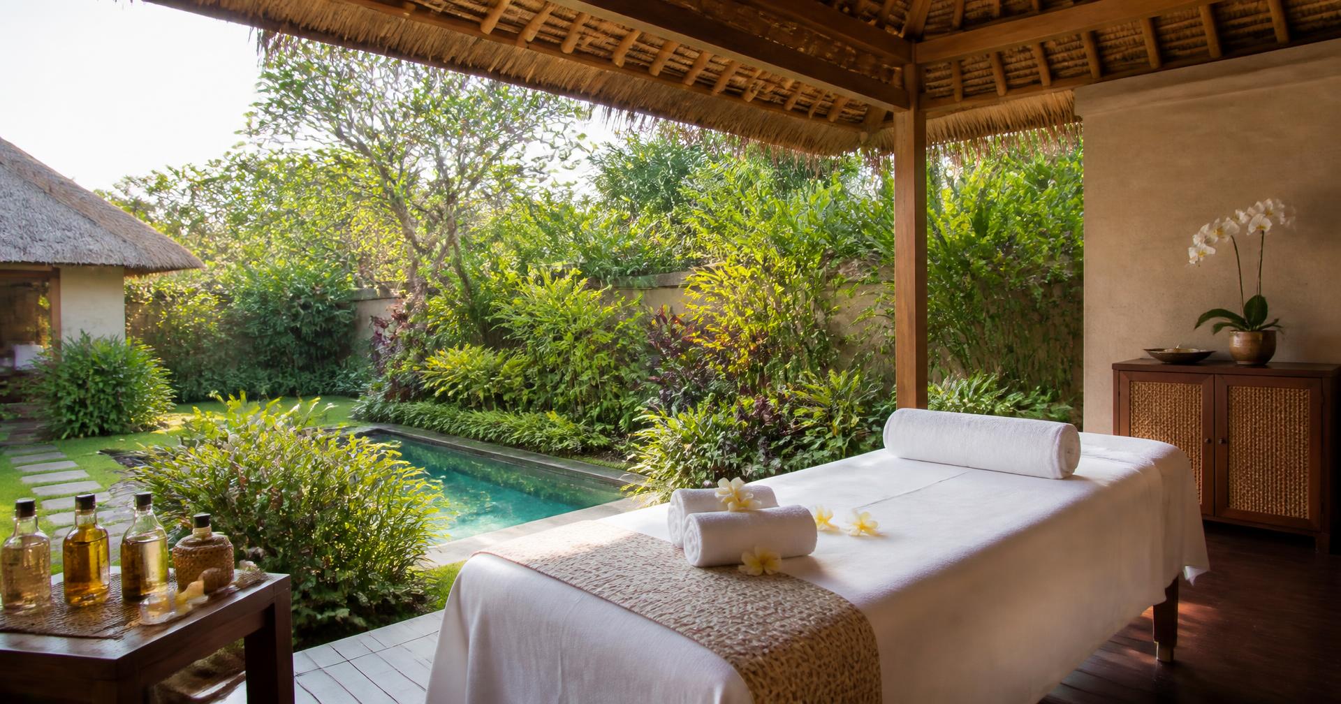 Open-air Balinese villa terrace with a prepared massage bed overlooking a tropical garden and pool